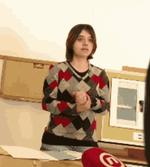a woman wearing a plaid sweater stands in front of a microphone with the letter e on it