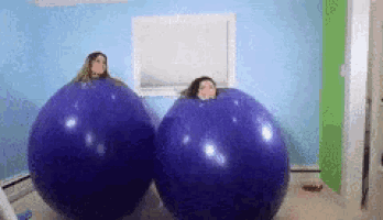two women are blowing up giant purple balloons .