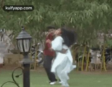 a man and a woman are dancing in a park with trees in the background .