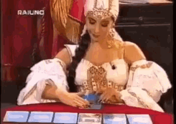 a woman in a white dress is sitting at a table with cards .