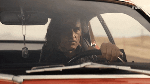 a man is driving a red car with the word max on the bottom right