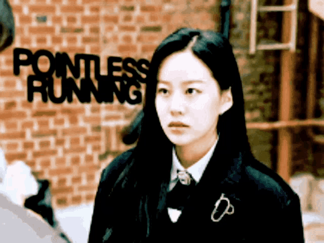 a girl stands in front of a brick wall with pointless running written on it