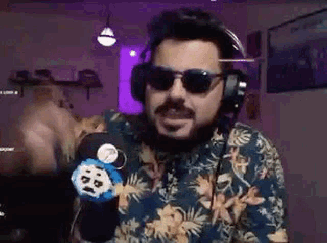 a man with a beard is wearing headphones and sunglasses while talking into a microphone .