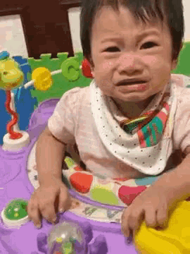 a baby is crying while sitting in a walker and playing with toys .