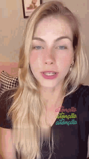 a woman with blonde hair and blue eyes is wearing a black shirt with a colorful embroidery on it .
