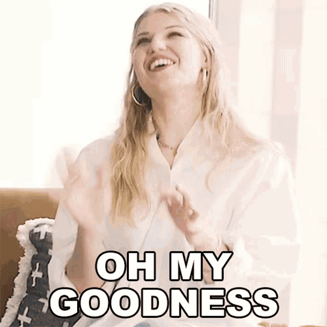 a woman is sitting on a couch with her hands up and says oh my goodness