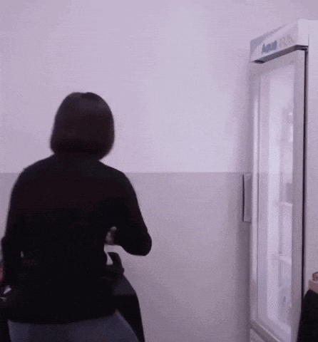 a woman in a black sweater is standing in front of a refrigerator .
