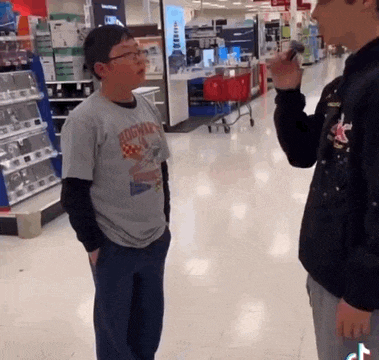 a boy wearing a hogwarts shirt is talking to another boy in a store .