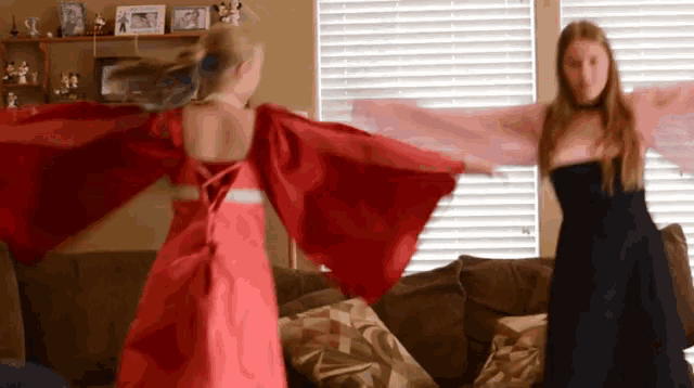two girls in dresses are dancing in a living room