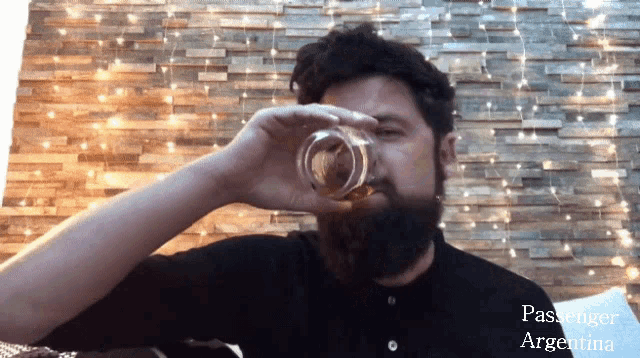 a man with a beard is drinking from a glass with the words passenger argentina written on the bottom