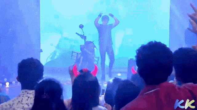 a group of people are watching a man on a stage with horns on their head and the letters kk on their back