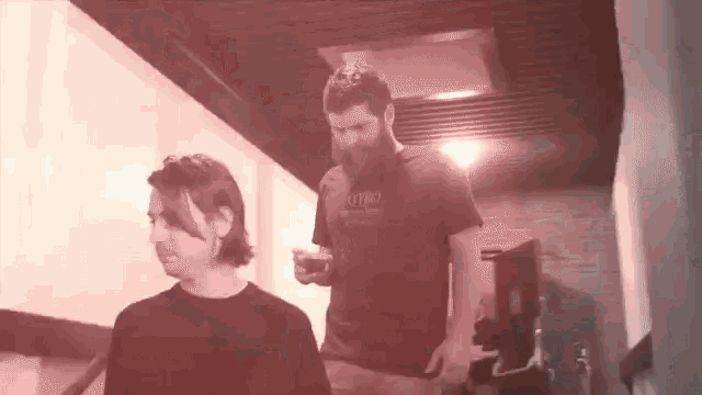 a man with a beard is standing next to another man with a gyro shirt on .