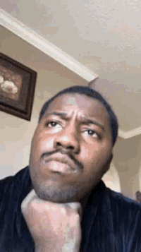 a man with a mustache has his hand on his chin and looks at the camera