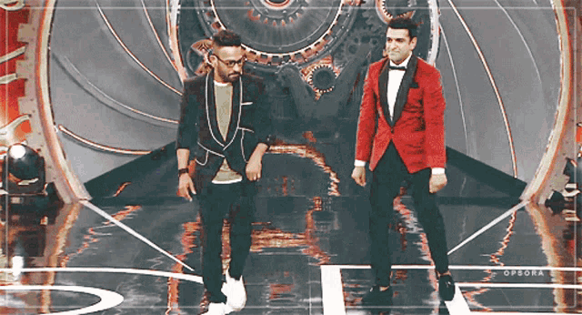 two men are standing on a stage and one is wearing a red suit