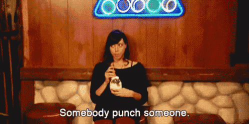 a woman is sitting in front of a neon sign that says ' somebody punch someone '