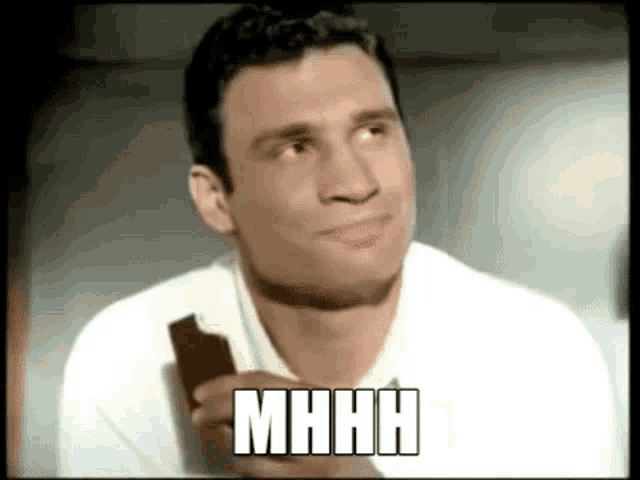 a man in a white shirt is holding a piece of chocolate and the word mhhh is above him