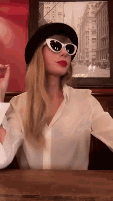 a woman wearing a black hat and white sunglasses is sitting at a table .