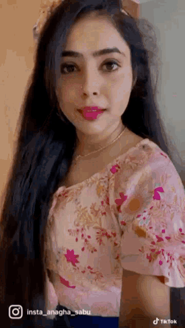 a woman with long hair is wearing a pink floral top and a necklace .