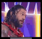 a man with a beard and a red lei around his neck is standing in front of a purple background .