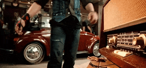 a man is fixing a car in a garage next to a radio and a beetle .