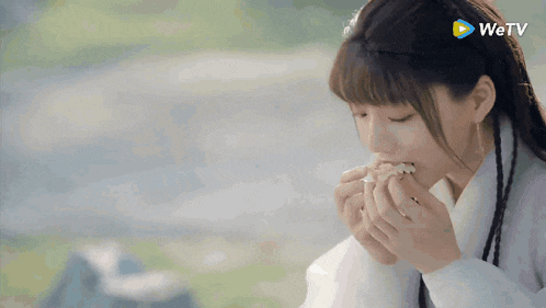 a woman is eating a piece of food with a wetv logo behind her