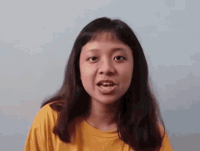 a young woman in a yellow t-shirt is talking to the camera .
