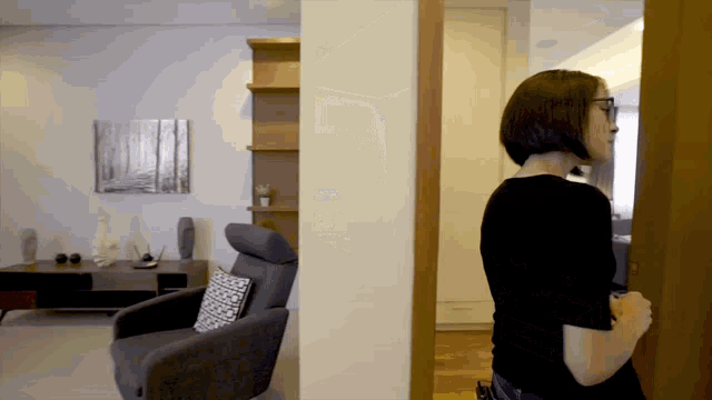 a woman standing in a living room looking at a chair
