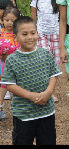 a boy wearing a green and blue striped shirt stands in a crowd of children