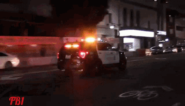 a police car is driving down a street at night with the letters pbi on the bottom right