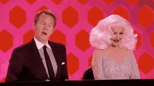 a man in a suit and tie and a woman in a wig are sitting next to each other .