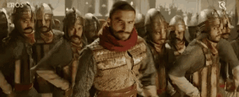 a man with a beard is standing in front of a group of soldiers wearing helmets .
