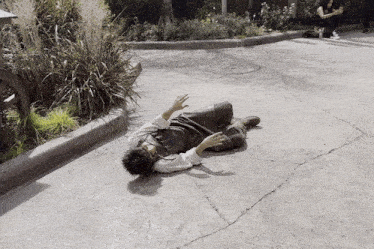 a man is laying on the ground while a woman sits on the sidewalk