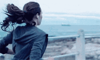 a woman wearing headphones is running on a beach near the ocean .