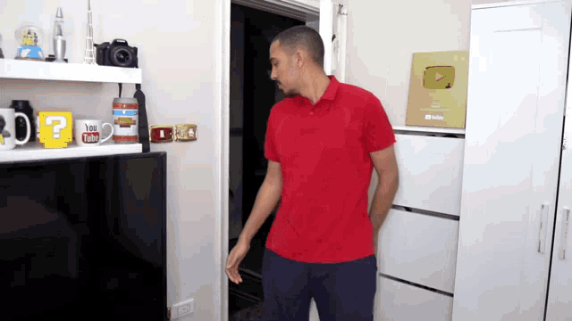 a man in a red shirt is standing in front of a shelf with a mug that says " you tube "