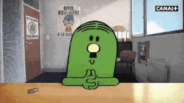 a green cartoon character is sitting at a table with his hands folded .