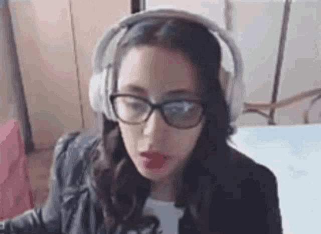 a woman wearing headphones and glasses is sitting in front of a computer screen .