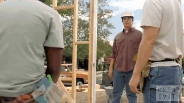 a group of construction workers are standing around a wooden structure .