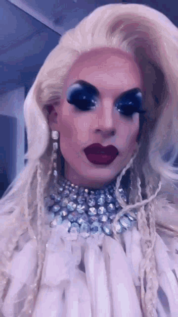 a drag queen wearing a white dress and a necklace