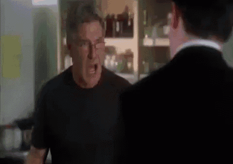 a man in a black shirt is yelling at another man in a black suit in a kitchen .