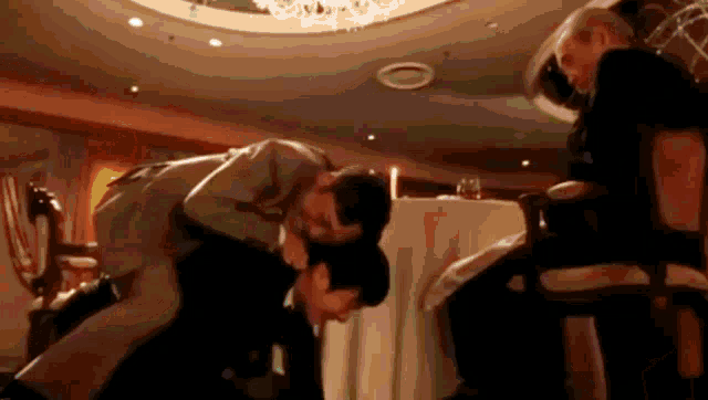 a man is kissing another man 's neck in a restaurant while another man sits in a chair .