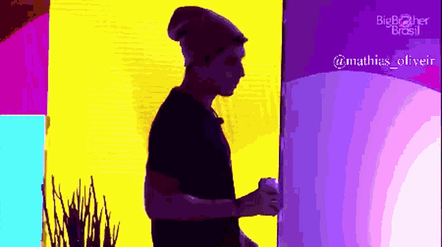 a man wearing a beanie is standing in front of a big brother brasil logo