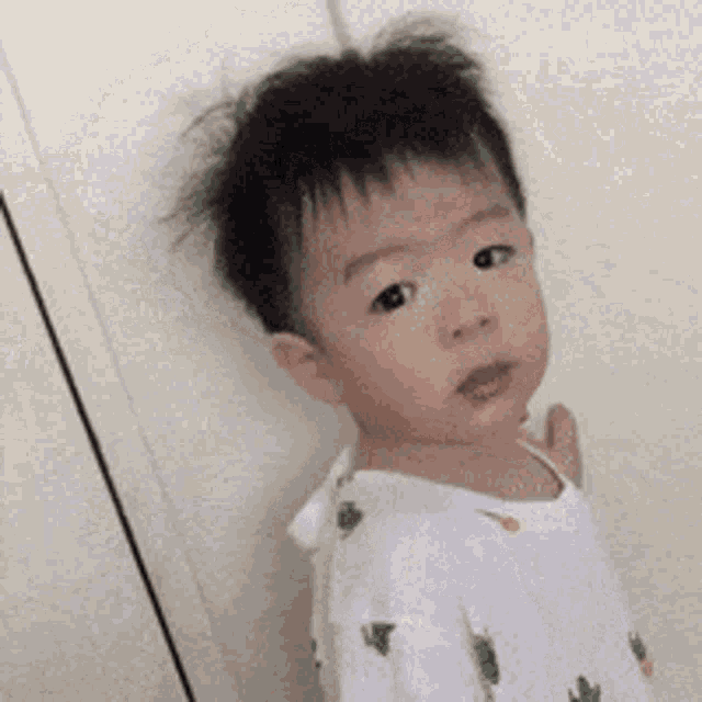 a baby is standing in front of a white wall .