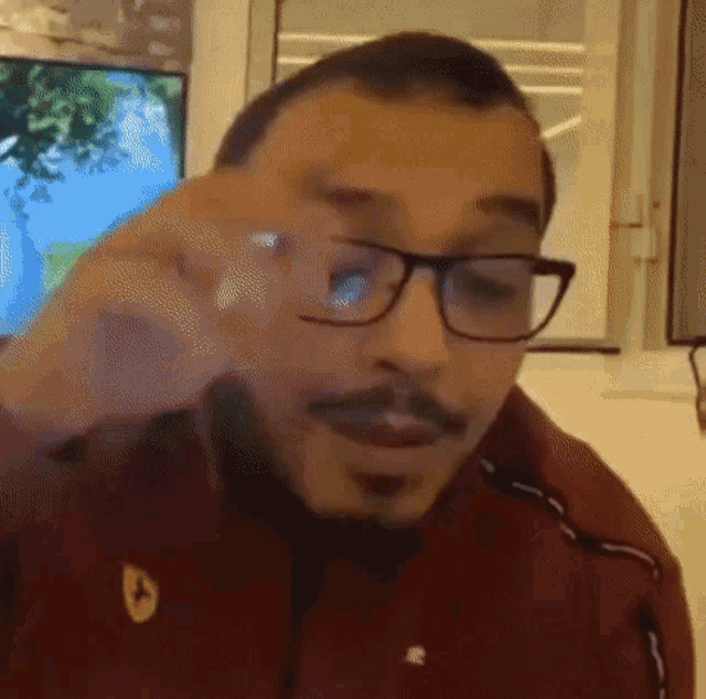 a man with glasses and a mustache is wearing a red jacket and making a funny face .