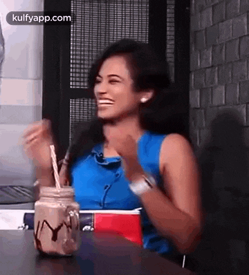 a woman is sitting at a table with a milkshake in a mason jar and laughing .