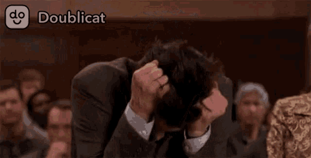 a man in a suit and tie is scratching his head in front of a crowd of people .