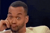 a man in a suit is making a funny face while holding his hand to his face .