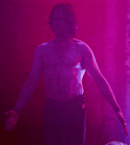 a man without a shirt is standing in a pink room