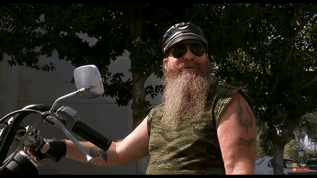a man with a beard wearing sunglasses and a hat is standing next to a motorcycle