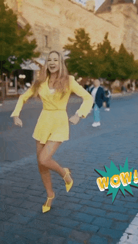 a woman in a yellow dress and yellow heels is dancing on a street with a wow sticker in the background