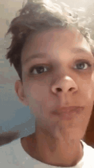 a close up of a young man 's face with a white shirt on making a funny face .